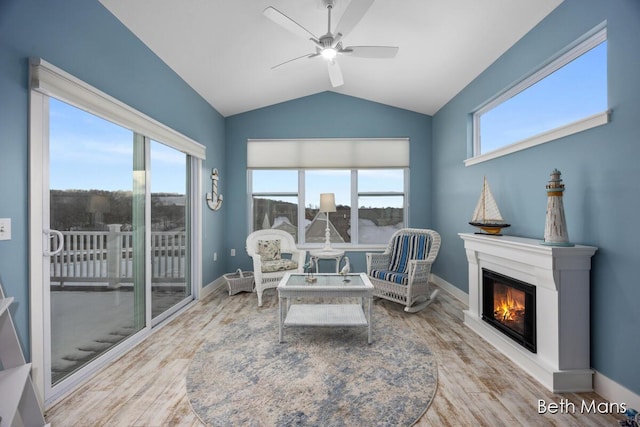 sitting room featuring a glass covered fireplace, wood finished floors, baseboards, ceiling fan, and vaulted ceiling