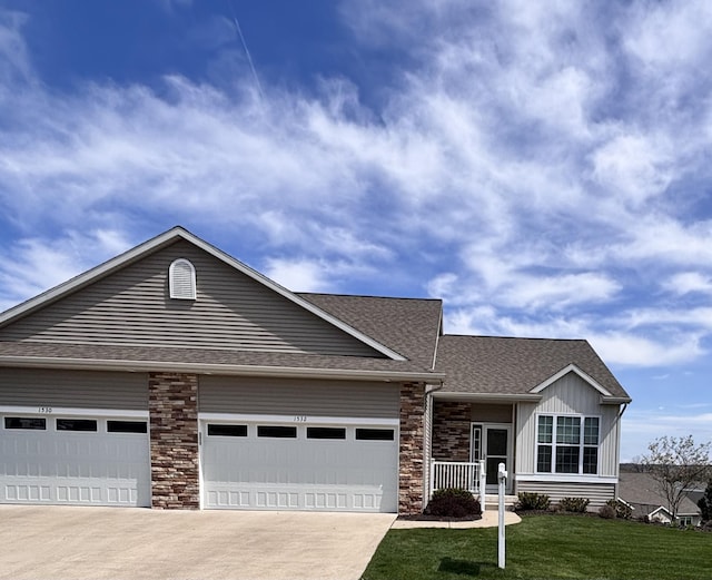 view of front facade featuring a front lawn, concrete driveway, an attached garage, a shingled roof, and stone siding