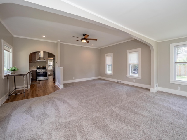 unfurnished living room with dark colored carpet, ceiling fan, and crown molding