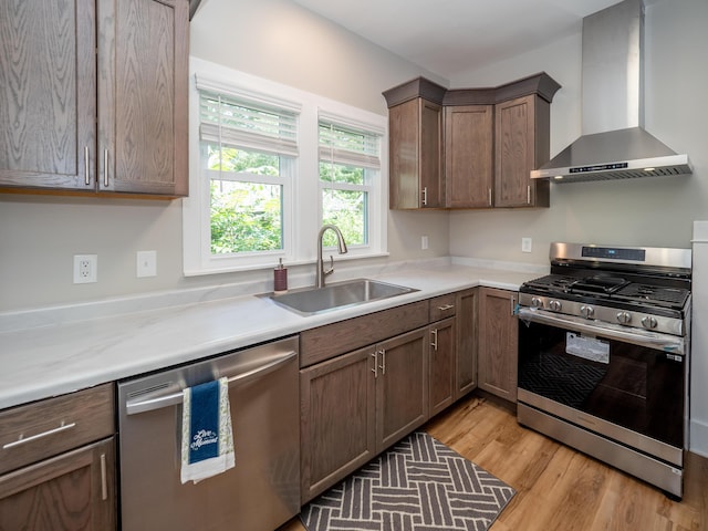 kitchen featuring appliances with stainless steel finishes, wall chimney exhaust hood, sink, and light wood-type flooring