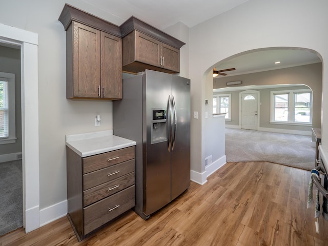 kitchen with crown molding, dark brown cabinetry, ceiling fan, stainless steel refrigerator with ice dispenser, and light hardwood / wood-style flooring