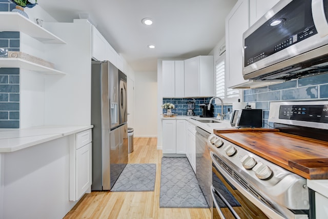 kitchen with sink, white cabinetry, appliances with stainless steel finishes, light hardwood / wood-style floors, and decorative backsplash