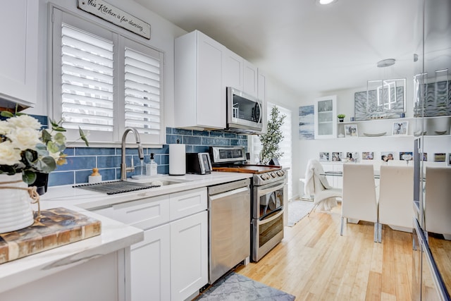 kitchen with sink, white cabinetry, hanging light fixtures, stainless steel appliances, and backsplash