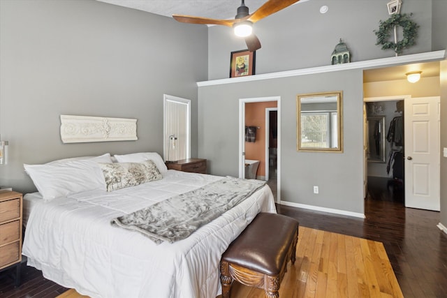 bedroom with ceiling fan, connected bathroom, dark hardwood / wood-style flooring, and a high ceiling