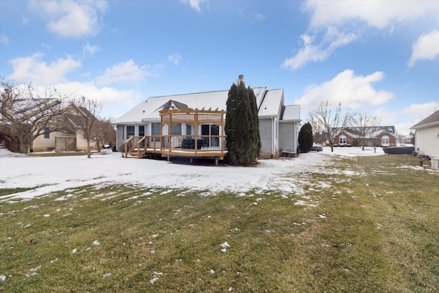 snow covered back of property with a wooden deck, a pergola, and a lawn