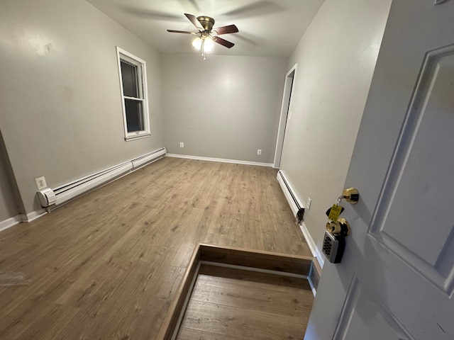 spare room featuring wood-type flooring, ceiling fan, and baseboard heating