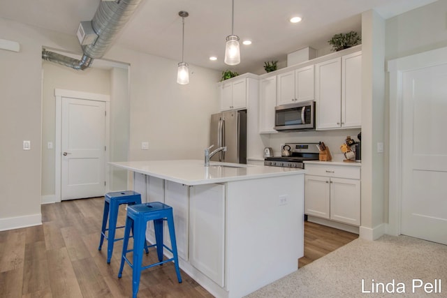 kitchen featuring hanging light fixtures, an island with sink, stainless steel appliances, light hardwood / wood-style floors, and white cabinets