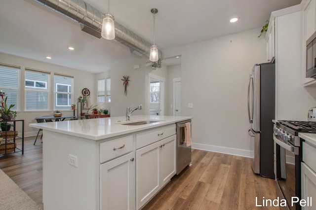 kitchen featuring sink, pendant lighting, stainless steel appliances, a kitchen island with sink, and white cabinets