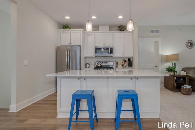 kitchen with white cabinetry, stainless steel appliances, a kitchen island with sink, and hanging light fixtures