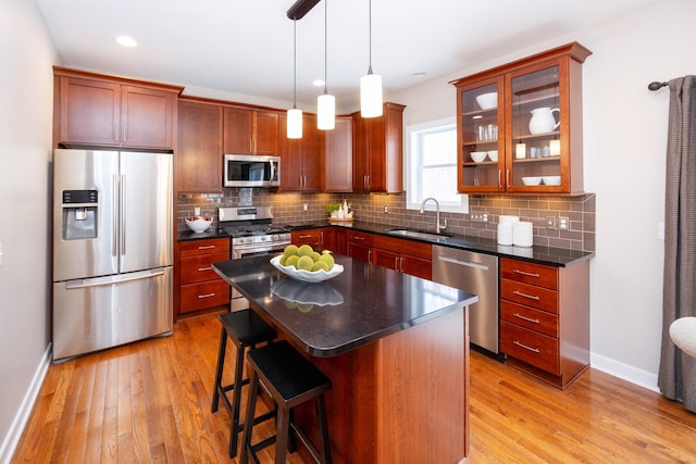 kitchen with sink, backsplash, stainless steel appliances, a kitchen island, and decorative light fixtures