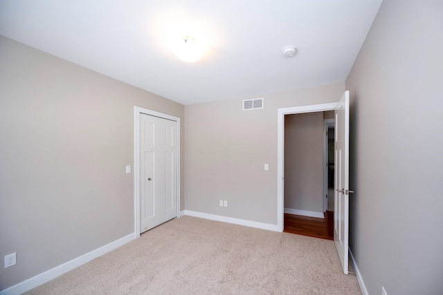 unfurnished bedroom with light colored carpet and a closet