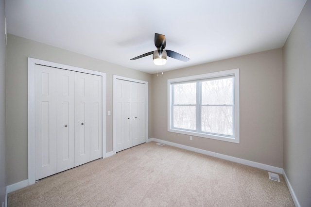 unfurnished bedroom featuring light carpet, two closets, and ceiling fan