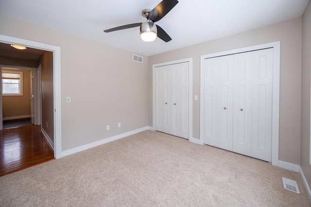 unfurnished bedroom with ceiling fan, multiple closets, and carpet