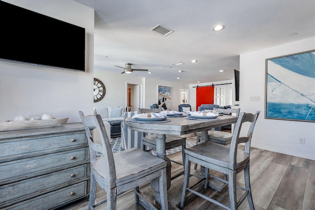 dining space featuring ceiling fan, a barn door, and light hardwood / wood-style floors