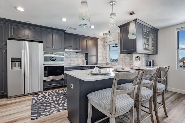 kitchen featuring hanging light fixtures, stainless steel appliances, a wealth of natural light, light hardwood / wood-style floors, and a kitchen island