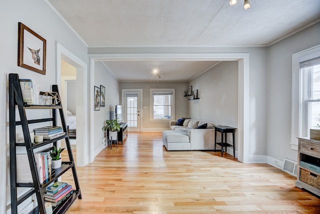 living room with light wood-type flooring, baseboards, visible vents, and ornamental molding