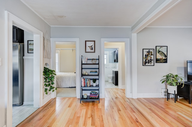 corridor with crown molding, light wood-style flooring, and baseboards