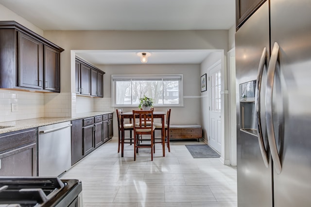 kitchen with stainless steel appliances, dark brown cabinetry, backsplash, and light stone counters