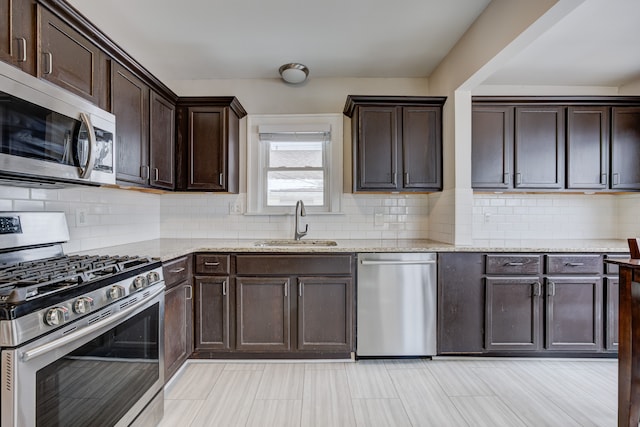 kitchen with light stone counters, stainless steel appliances, backsplash, a sink, and dark brown cabinets