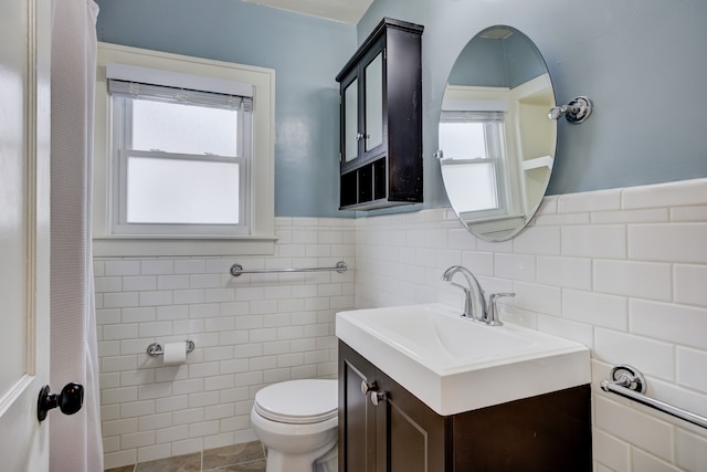 bathroom featuring a healthy amount of sunlight, toilet, tile walls, and vanity