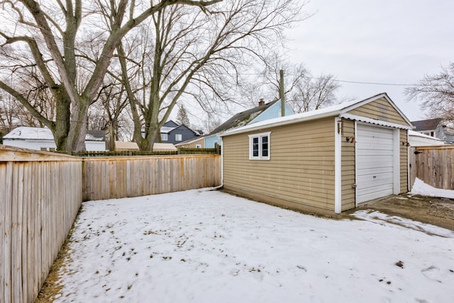 yard layered in snow with a garage, a fenced backyard, and an outdoor structure