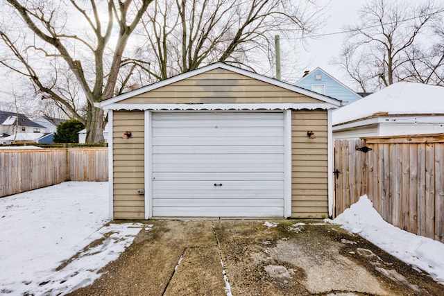 snow covered garage featuring fence, driveway, and a detached garage