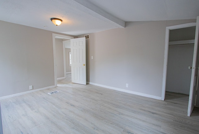 unfurnished bedroom with beam ceiling, a walk in closet, light hardwood / wood-style floors, and a closet