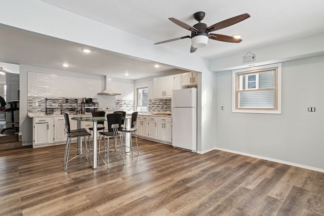 kitchen featuring white cabinetry, backsplash, custom range hood, a kitchen bar, and white fridge