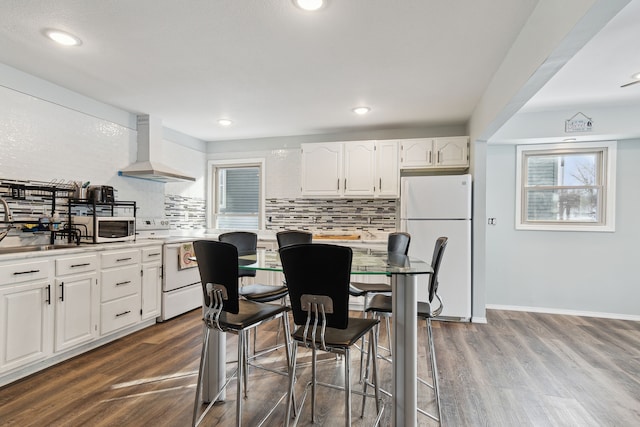 kitchen featuring white appliances, hardwood / wood-style floors, custom range hood, white cabinets, and decorative backsplash