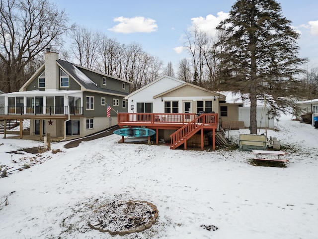 snow covered property featuring a sunroom, a deck, and an outdoor fire pit