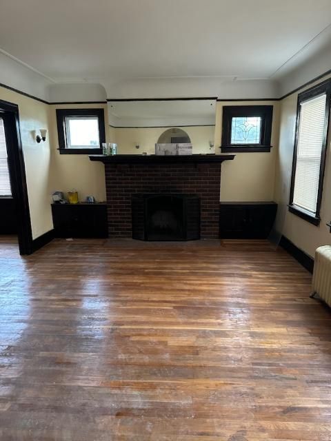 unfurnished living room with radiator heating unit, ornamental molding, a brick fireplace, and hardwood / wood-style floors