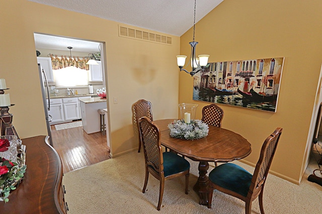 carpeted dining room with sink, vaulted ceiling, a textured ceiling, and a notable chandelier