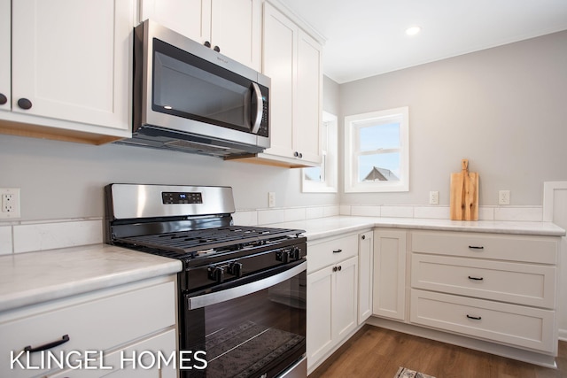 kitchen with appliances with stainless steel finishes, dark hardwood / wood-style flooring, light stone countertops, and white cabinets