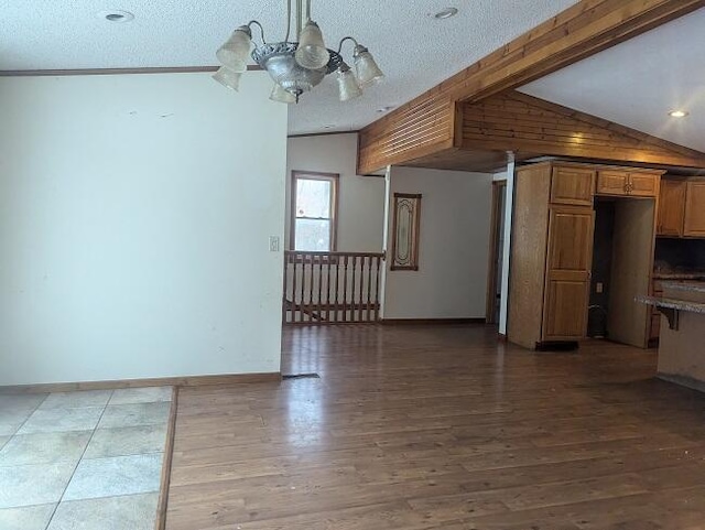 unfurnished living room with a notable chandelier, wood-type flooring, a textured ceiling, and vaulted ceiling with beams