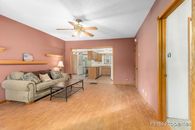 living room featuring ceiling fan, a textured ceiling, and light hardwood / wood-style floors