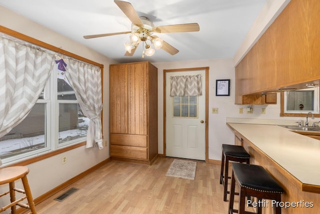 interior space featuring sink, light hardwood / wood-style flooring, a breakfast bar, ceiling fan, and kitchen peninsula