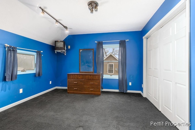 unfurnished bedroom featuring vaulted ceiling, track lighting, a closet, and dark colored carpet