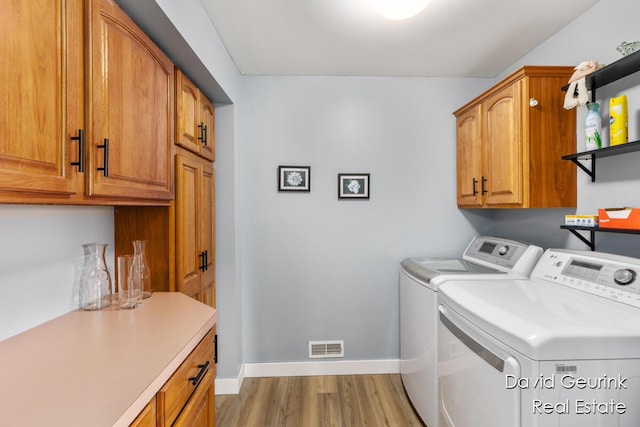 laundry room with cabinets, washer and clothes dryer, and light hardwood / wood-style floors