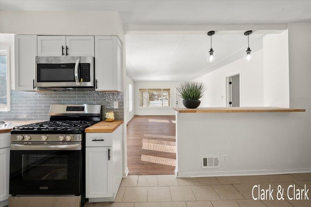 kitchen featuring butcher block counters, pendant lighting, stainless steel appliances, and white cabinets