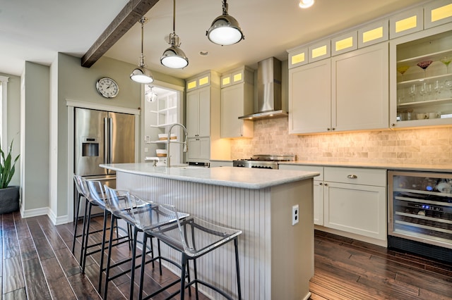 kitchen with wine cooler, high end fridge, sink, an island with sink, and wall chimney range hood