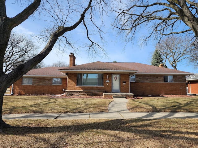 single story home featuring brick siding, a chimney, and a front lawn