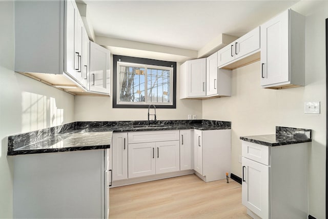 kitchen with dark stone countertops, sink, white cabinets, and light wood-type flooring