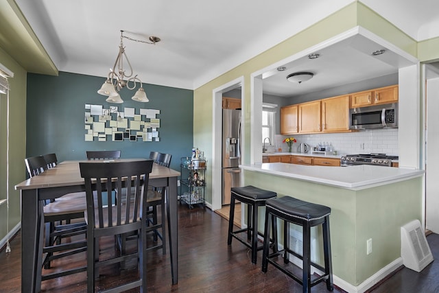 kitchen with sink, tasteful backsplash, appliances with stainless steel finishes, dark hardwood / wood-style floors, and pendant lighting