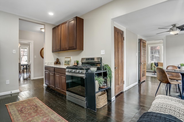 kitchen featuring dark wood-type flooring, stainless steel gas range oven, dark brown cabinets, and ceiling fan