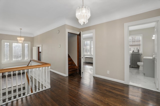 empty room with dark wood-type flooring, a healthy amount of sunlight, radiator, and a notable chandelier