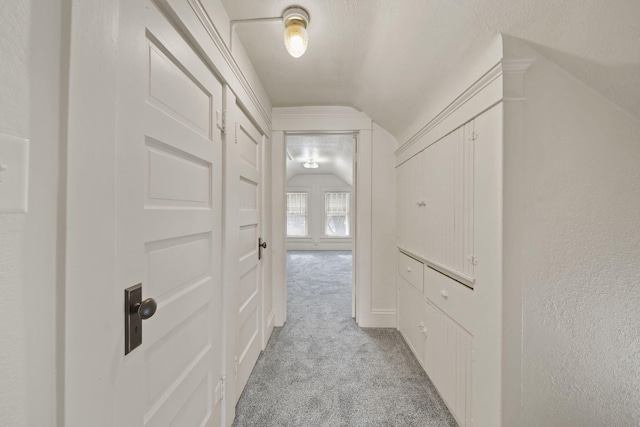 hallway with light carpet, vaulted ceiling, and a textured ceiling