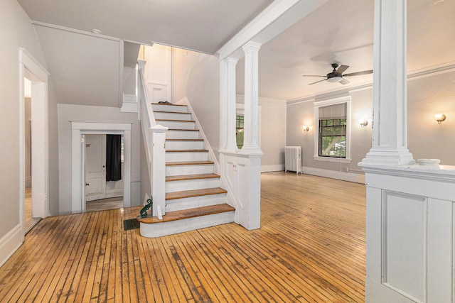 stairway with ceiling fan, wood-type flooring, radiator, and decorative columns