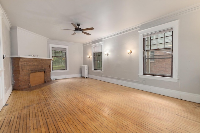 unfurnished living room with radiator, light hardwood / wood-style flooring, ceiling fan, ornamental molding, and a brick fireplace