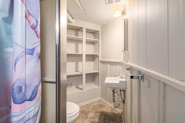 bathroom featuring toilet, sink, and wood walls