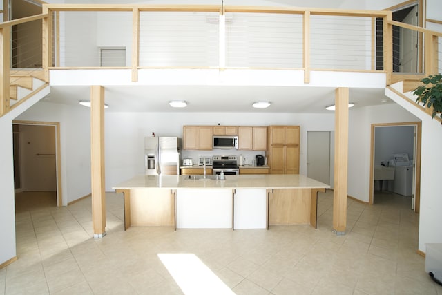 kitchen with washing machine and clothes dryer, light brown cabinetry, a breakfast bar, sink, and appliances with stainless steel finishes